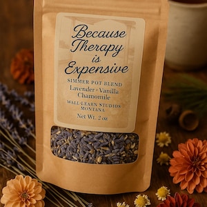May include: A brown paper bag of simmer pot blend with a clear window, featuring the text "Because Therapy is Expensive." The blend includes lavender, vanilla, and chamomile. The net weight is 2 oz. Decorative flowers and lavender sprigs surround the bag.