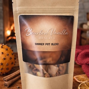 May include: A brown paper bag with a clear window displaying a simmer pot blend. The bag has the words "Bourbon Vanilla RESERVE SIMMER POT BLEND" printed on it. Cinnamon sticks, star anise, and dried orange slices are visible.