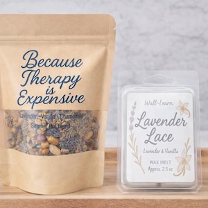 May include: A kraft paper bag with the text "Because Therapy is Expensive" and a clear window showing a simmer pot blend. Next to it is a wax melt package labeled "Lavender Lace" with lavender and vanilla scent.