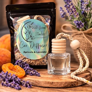 May include: A car air freshener with a clear, square glass bottle and a wooden top. The label reads "Car Diffuser Apricots & Lavender." A bag of dried botanicals and lavender sprigs are also visible.