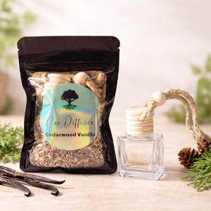 May include: A car air freshener set featuring a clear glass bottle with a wooden cap and a bag of cedarwood vanilla fragrance. The bag has a holographic label with the text "Car Diffuser" and "Cedarwood Vanilla".
