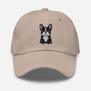 May include: A tan baseball cap featuring an embroidered black and white French Bulldog design. The cap has a curved brim and an adjustable strap at the back, offering a classic, casual style.
