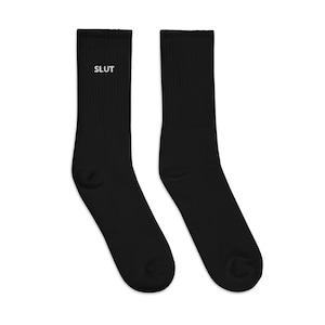 May include: A pair of black crew socks with the word "SLUT" embroidered in white on one sock.