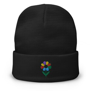 Può includere: Un berretto nero con un motivo floreale ricamato colorato. Il fiore presenta petali rossi, gialli, blu, verdi e viola. Il cappello è realizzato in morbido materiale a maglia.