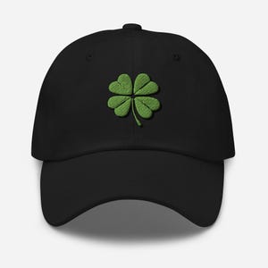 Può includere: Un cappello da baseball nero con un quadrifoglio verde ricamato.