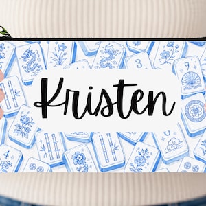 May include: A rectangular zippered pouch featuring a white and blue pattern of Mahjong tiles with floral, dragon, and bamboo motifs. A central white horizontal label displays the name Kristen in a black, cursive, handwritten-style font.