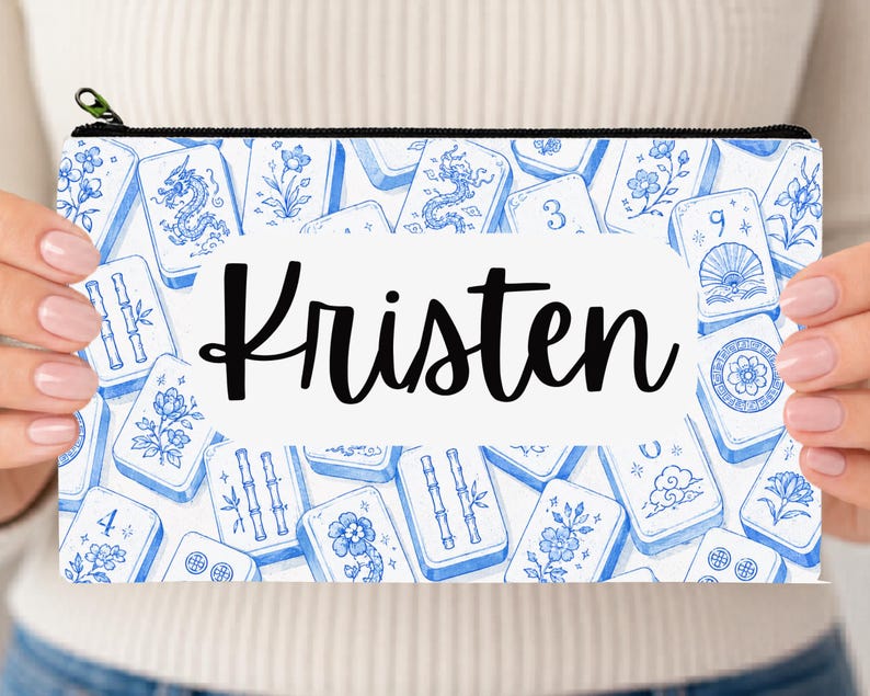 May include: A rectangular zippered pouch featuring a white and blue pattern of Mahjong tiles with floral, dragon, and bamboo motifs. A central white horizontal label displays the name Kristen in a black, cursive, handwritten-style font.