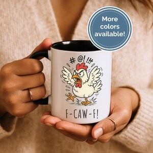 May include: White ceramic mug with a black handle and interior, featuring an angry cartoon chicken illustration. The mug has the text "# @! !!" above the chicken and "F-CAW-FI" below. A blue circle with the text "More colors available!" is in the background.