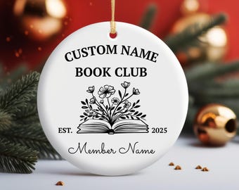 Peut inclure: Une décoration ronde en céramique blanche avec le texte noir CUSTOM NAME BOOK CLUB et Member Name, un graphique central d'un livre ouvert avec des fleurs et le texte EST. 2025. Une ficelle dorée est attachée au sommet pour la suspension.