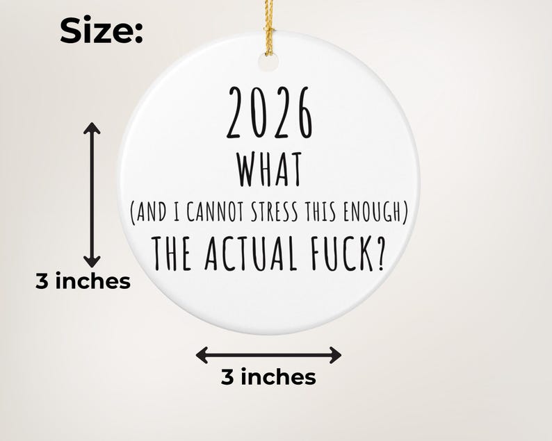 May include: A white ceramic ornament with the text "2026 WHAT (AND I CANNOT STRESS THIS ENOUGH) THE ACTUAL FUCK?" in black. The ornament is 3 inches in diameter and has a gold string for hanging.