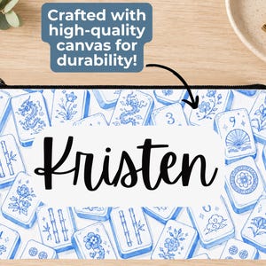 May include: A rectangular canvas zipper pouch featuring a blue and white pattern of mahjong tiles with various floral, dragon, and numerical designs. The center of the pouch displays the name Kristen in a black script font on a white background.