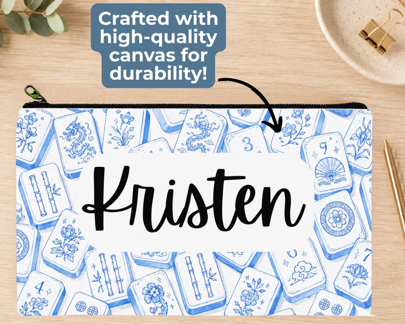 May include: A rectangular canvas zipper pouch featuring a blue and white pattern of mahjong tiles with various floral, dragon, and numerical designs. The center of the pouch displays the name Kristen in a black script font on a white background.