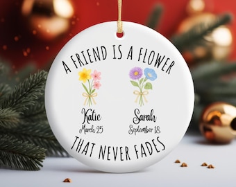 May include: A round white ceramic ornament featuring the black text A FRIEND IS A FLOWER THAT NEVER FADES. It displays two floral bouquets with yellow, pink, purple, and blue flowers, personalized with the names Katie and Sarah and dates.