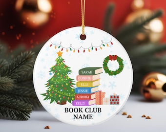 Peut inclure: Une décoration ronde en céramique blanche ornée d'un sapin de Noël vert, d'une couronne et d'une pile de six livres colorés portant les noms Sarah, Connie, Elle, Jessie, Aurora et Kelly. Sous les livres, le texte indique BOOK CLUB NAME.