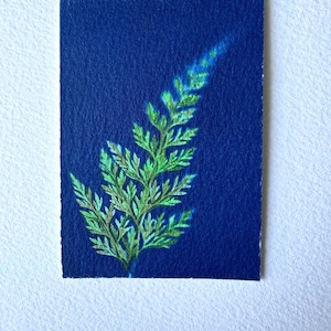 May include: A rectangular painting on textured paper featuring a single fern frond rendered in shades of vibrant green and yellow against a deep, solid navy blue background. The botanical illustration displays intricate leaf details.