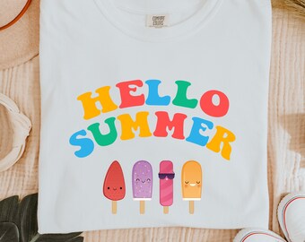 May include: White t-shirt with the text "HELLO SUMMER" in rainbow colors. Below the text are four cartoon popsicles with happy faces.