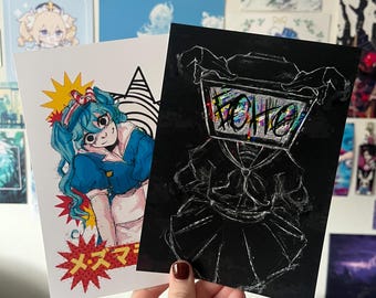 Puede incluir: Dos ilustraciones impresas en cartulina. La primera ilustración es un personaje de estilo anime colorido con cabello azul y un lazo rojo y blanco. La segunda ilustración es un dibujo en blanco y negro de una figura con una televisión por cabeza. El texto "メスマ" está impreso en la primera ilustración.