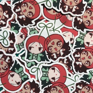 May include: A collection of stickers featuring a cartoon character with a cherry-like design. The character has a red cherry-shaped hat, brown hair, and a smiling face. The stickers are on a white background with green stems.