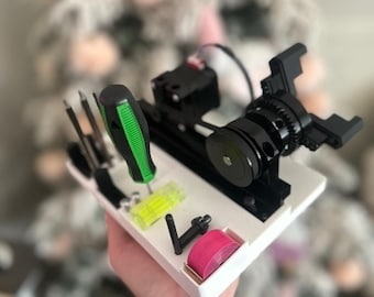 May include: A white 3D printed organizer with a black and silver motor, a green screwdriver, a yellow and green level, and a pink roll of tape.