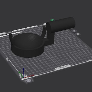 May include: A black 3D-printed object, possibly a component or tool, is positioned on a grid-patterned surface. The object has a circular base with a handle and a cylindrical extension. The surface has text that reads "Creality Smart PEI Plate".