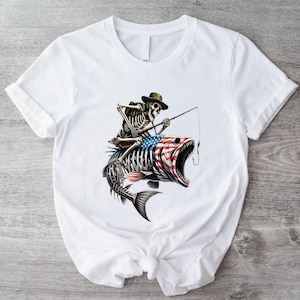 Puede incluir: Camiseta blanca con un gráfico de un esqueleto con un sombrero y pescando desde un pez con un diseño de bandera estadounidense.