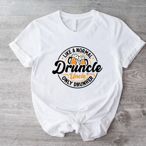 May include: White t-shirt with a black circle graphic that says "Like a normal uncle, only drunker" with a beer mug graphic inside the circle. The text "Druncle" is in a stylized font.