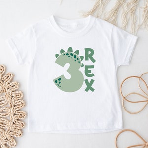 May include: White t-shirt with a green dinosaur-shaped number 3 and the word "REX" in green letters.