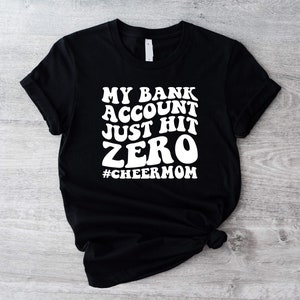 Puede incluir: Camiseta negra con texto blanco que dice "Mi cuenta bancaria acaba de llegar a cero #cheermom".