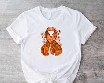May include: White t-shirt featuring an orange awareness ribbon and boxing gloves design. The graphic includes floral accents. The shirt is made of a soft material and has a classic crew neck.