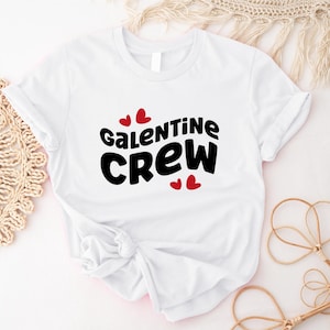 Puede incluir: Camiseta blanca con el texto "Galentine Crew" en negro con corazones rojos.
