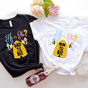 Könnte beinhalten: Zwei Gender-Reveal-T-Shirts mit einem Bienenstock-Design. Das schwarze Shirt sagt "He or She? Dad to Bee" und das weiße Shirt sagt "He or She? Mom to Bee".