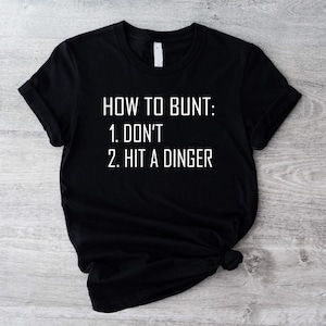 May include: Black t-shirt with white text that reads "How to Bunt: 1. Don't 2. Hit a Dinger"