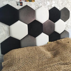 May include: A contemporary headboard featuring hexagonal panels in black, white, and grey. The panels are arranged in a geometric design against a textured wall. A brown knitted blanket is in the foreground.