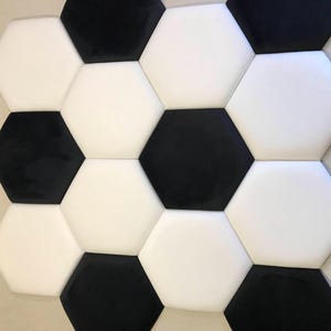 May include: A close-up of a wall panel featuring a soccer ball design. The panel is made up of black and white hexagonal shapes, forming a traditional soccer ball pattern. The contrasting colours and geometric design give the panel a modern appearance.