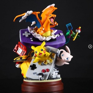 May include: A detailed figurine featuring several Pokémon characters, including Charizard, Pikachu, and Mew, with a purple handheld game console base. The figurine has a wooden base and is set against a dark background.