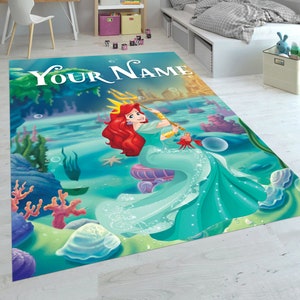 Puede incluir: Una alfombra azul y verde con una imagen de dibujos animados de Ariel, la Sirenita, sosteniendo un tridente. La alfombra tiene el texto "YOUR NAME" en la parte superior.