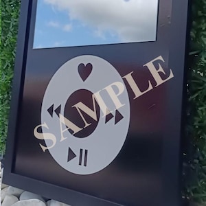 May include: Black framed wall art with a mirror and a white graphic of a music player control. The graphic includes a heart, play, and pause symbols. The word "SAMPLE" is printed across the graphic.