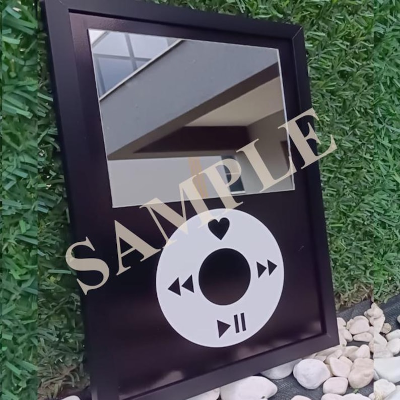 May include: Black framed mirror with a white circular design featuring a heart, play, pause, and skip buttons. The word "SAMPLE" is printed across the mirror. The mirror is rectangular and set against a green grassy background.