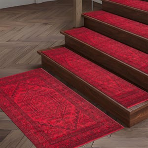 Może przedstawiać: Czerwone stopnie schodów i pasujący prostokątny dywan z ciemnym, szczegółowym wzorem. Stopnie są zamontowane na drewnianych schodach. Dywan leży na podłodze przed schodami. Dywan i stopnie mają postarzany wygląd.