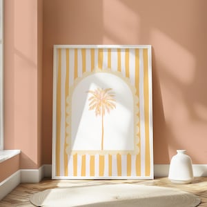 May include: A framed print with a yellow and white striped background. A white archway with a scalloped edge surrounds a palm tree illustration in shades of orange and pink.