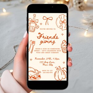 Peut inclure: Un smartphone affiche une invitation de Thanksgiving avec des illustrations orange sur fond crème. Le texte dit "Friends giving" et comprend une date, une heure et des informations RSVP. Le design présente des éléments festifs et de la nourriture.