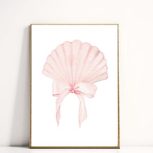 May include: A framed watercolor print featuring a light pink seashell with a delicate bow. The seashell has a fan-like shape with detailed ridges. The bow is tied at the base of the shell, with long, flowing ribbons. The artwork is set against a white background.