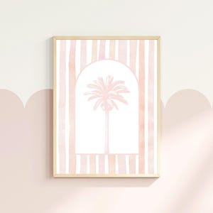 May include: A framed art print featuring a pink palm tree within an archway, set against a backdrop of vertical pink and white stripes. The artwork is displayed on a light pink wall.
