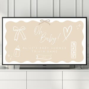 Peut inclure: Un écran de télévision affiche un jeu de questions pour une baby shower. L'écran présente les mots "Oh Baby!" en cursive, ainsi que des illustrations sur le thème des bébés. Le jeu est pour la baby shower d'Alice et comporte un bouton "Start".