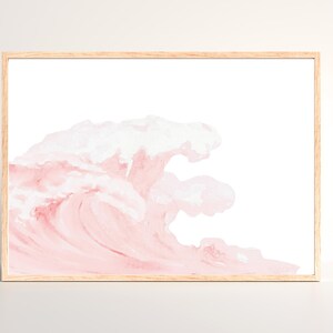 May include: Watercolor print of a wave in shades of pink and white, framed in a light wood frame. The artwork depicts a stylized ocean wave, with soft brushstrokes creating a sense of movement and texture. A decorative piece for home decor.