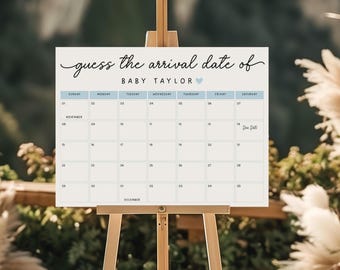 Op de afbeelding: Een witte kalender op een houten ezel met de tekst "guess the arrival date of BABY TAYLOR". Het kalenderraster is lichtblauw met data voor november en december. Er staat een hartpictogram naast de naam.