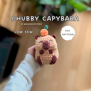 May include: A crocheted capybara plushie with a pumpkin on its head. The plushie is tan with dark brown accents and a smiling face. Text on the image reads "CHUBBY CAPYBARA", "LOW SEW", and "PDF PATTERN".