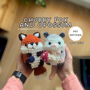 以下が含まれることがあります： 手作りの編みぐるみ2体：キツネとオポッサム。キツネはオレンジ、茶色、白で、オポッサムはグレー、白、ピンクです。キツネは青いボールを持っており、オポッサムはキノコを持っています。「CHUBBY FOX AND OPOSSUM」と「PDF PATTERN LOW SEW」というテキストがあります。