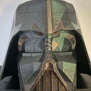 May include: A black and green 3D printed Darth Vader helmet with a geometric design.