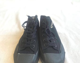 May include: A pair of black high-top sneakers. The sneakers have black laces, a rubber toe cap, and a textured rubber sole. The canvas material is a solid black color. The shoes are displayed on a white surface.